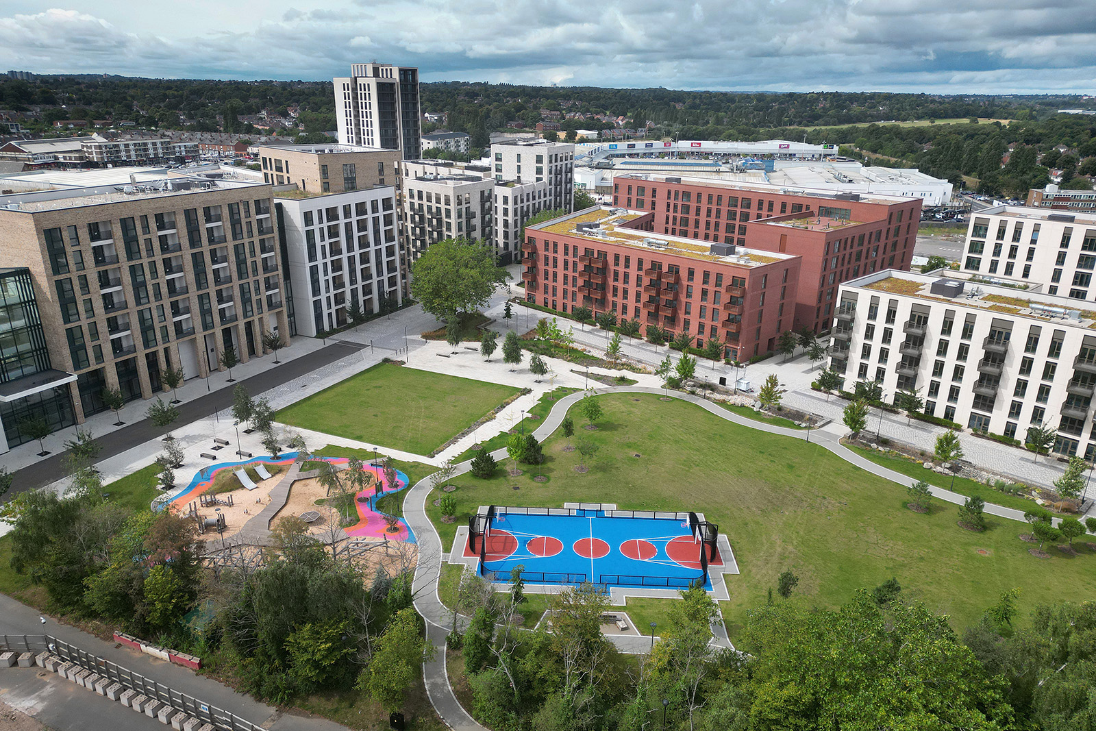 An aerial view of white, red and beige medium-rise blocks surrounding a green space containing a swimming pool