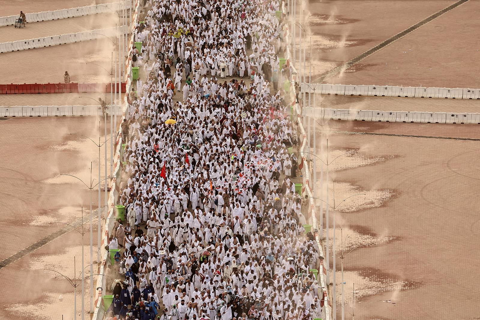 A photograph of a column of hundreds of pilgrims, walking between columns spraying water to keep them cool in the heat, as they arrive to perform the symbolic stoning of the three Jamarat in Mina, June 2024