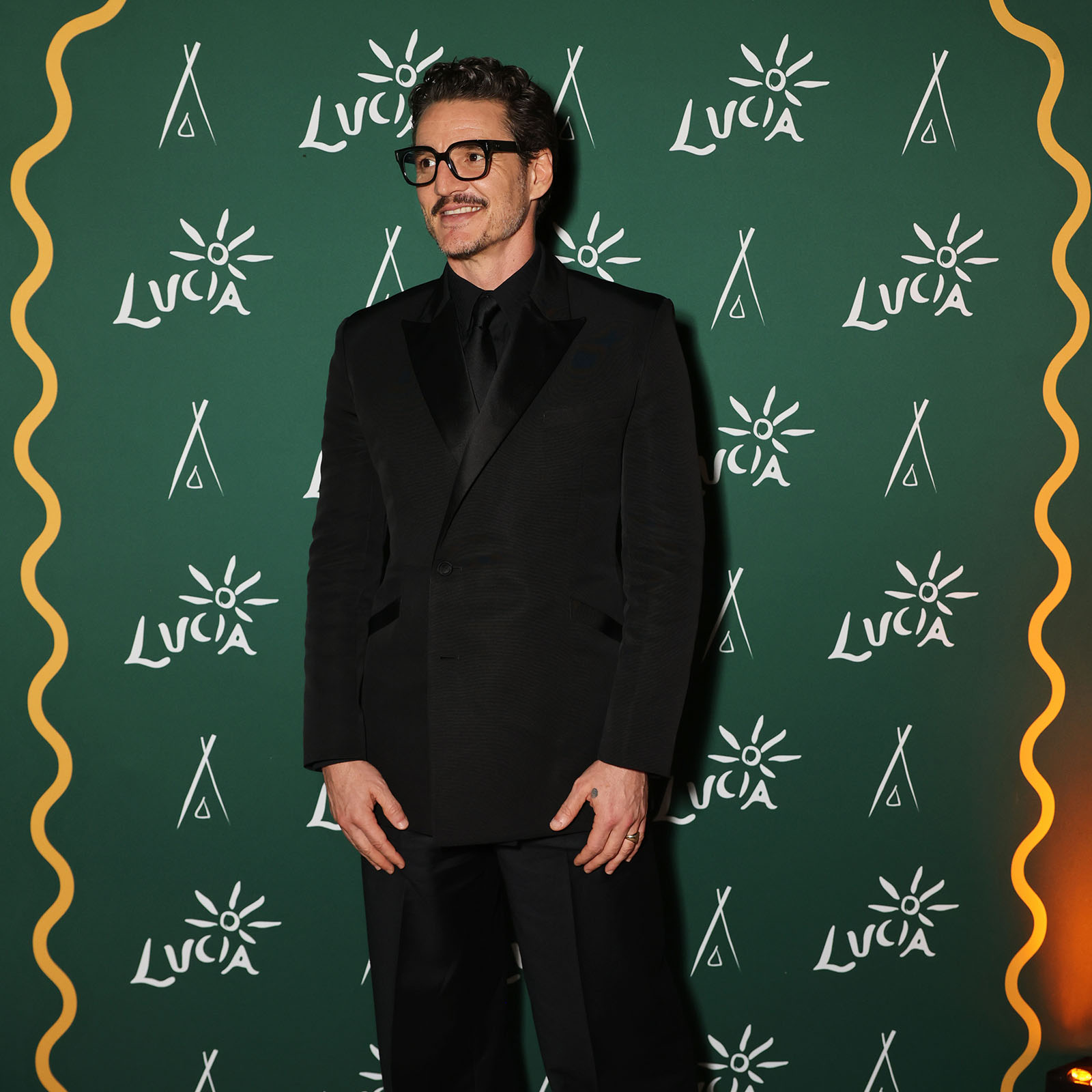 A photograph of Pedro Pascal, wearing a black shirt, tie and suit and posing for the cameras, at the Eddington after party during the 2025 Cannes Film Festival