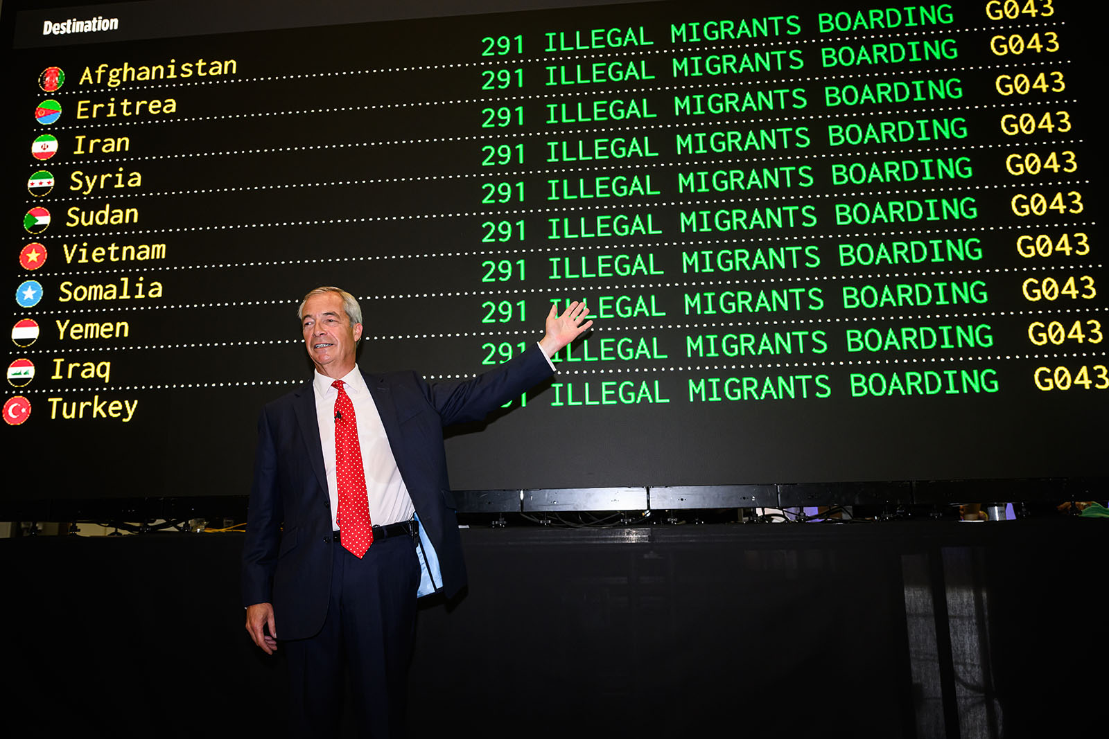 Nigel Farage in a suit gestures at a fake departures board listing countries and the message '291 ILLEGAL MIGRANTS BOARDING' for each one