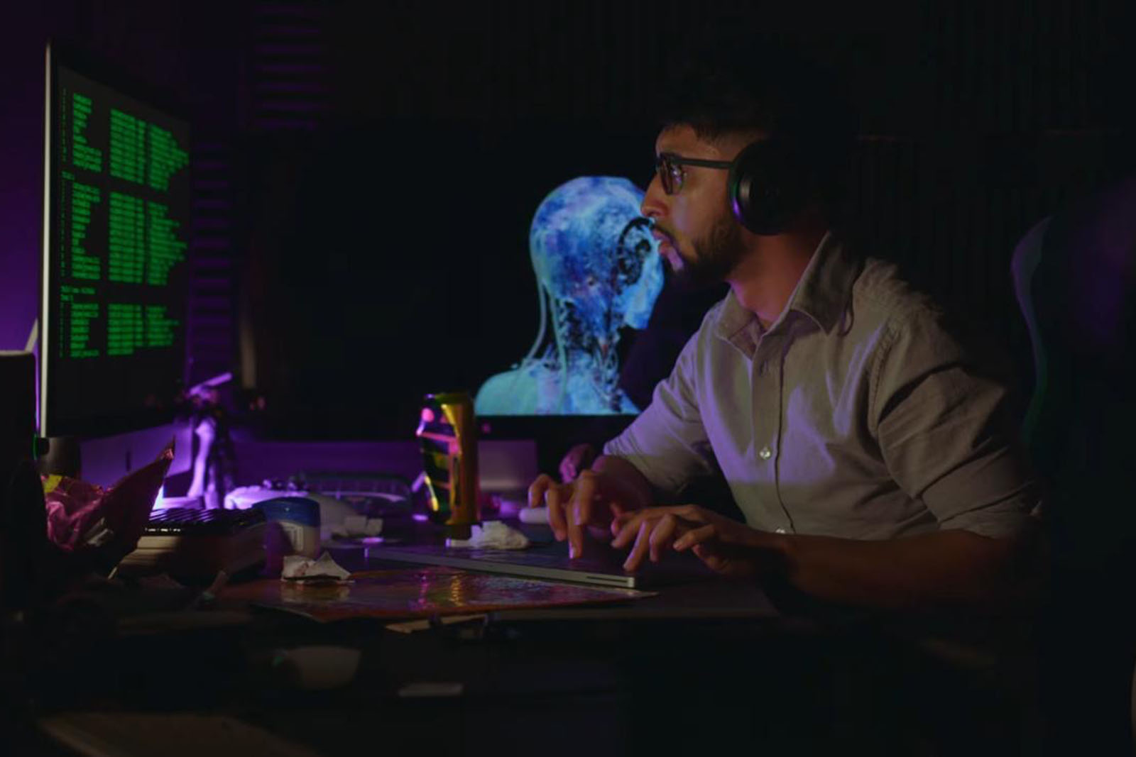 A still image from a short teaser video for Smash Bengali's film project Get Khan Home, featuring the comedian as the lead character, sitting in a darkened room looking at a computer screen