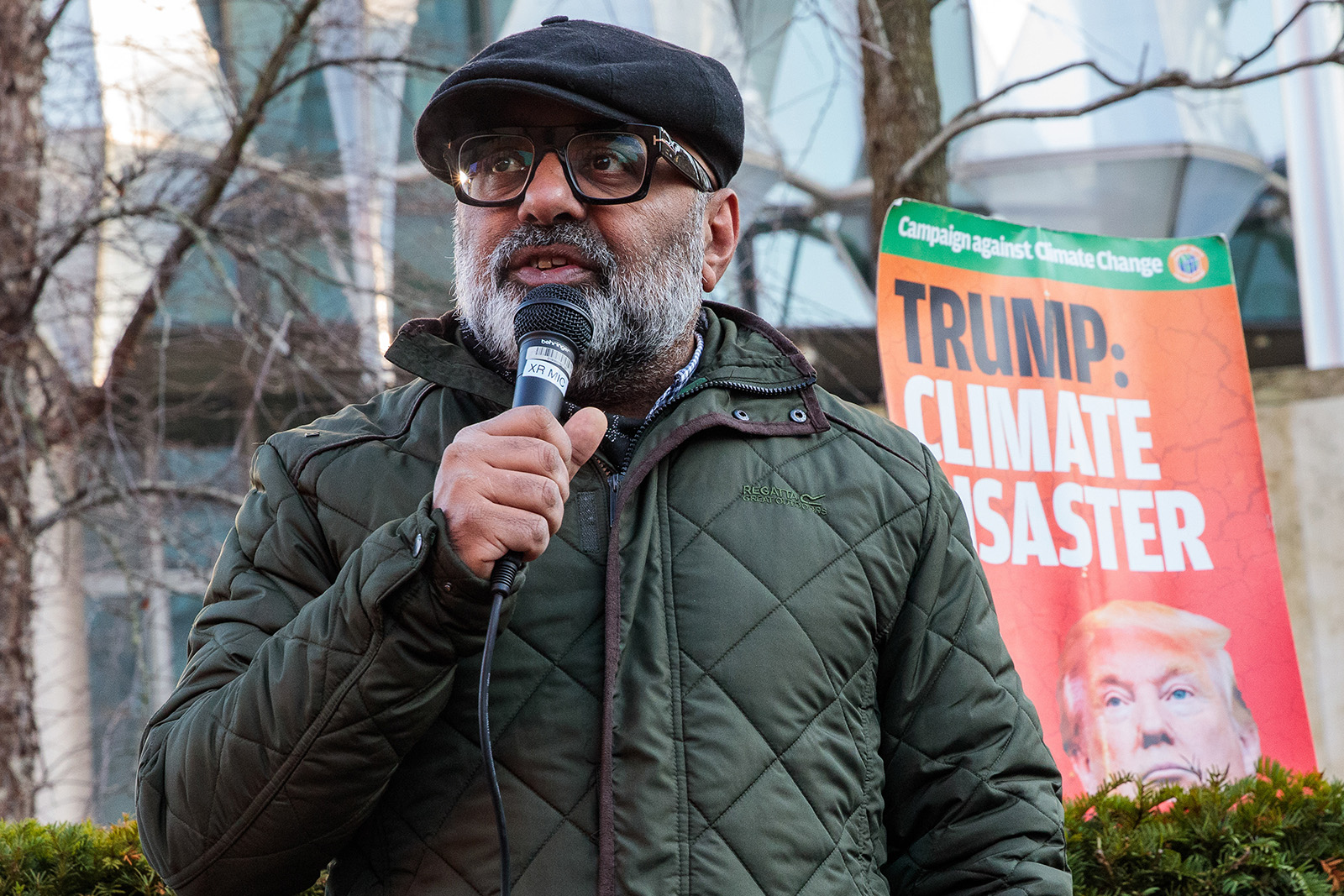 A photograph of Asad Rehman, as head of War On Want and wearing a hat and coat, addresses protestors outside the US embassy in London shortly before Donald Trump returned to the White House, January 2025