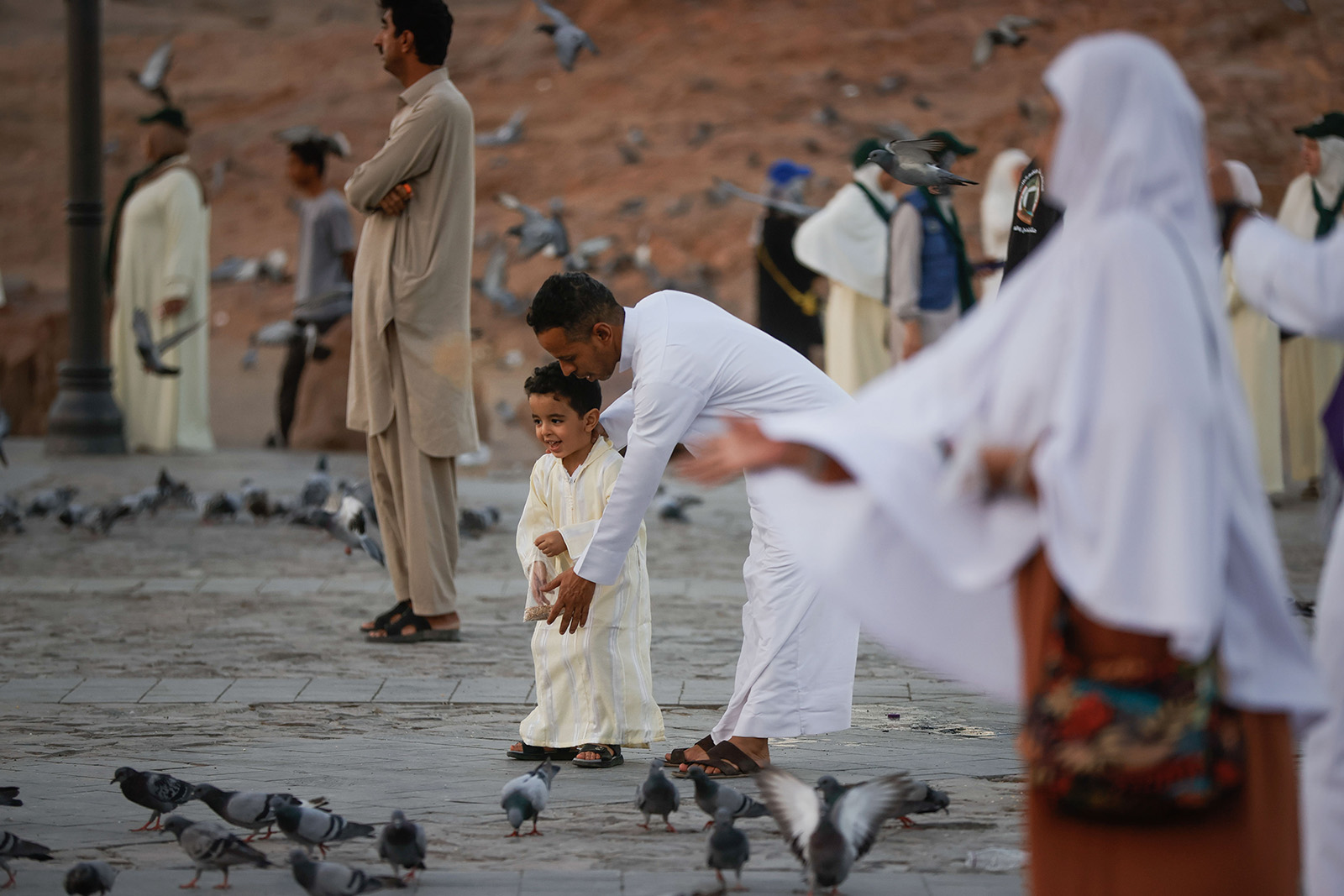 An image of pilgrims visiting Mount Uhud as they continue their spiritual journey outside Medina after completing the Hajj in Mecca, June 2025. In the centre of the photo, a father and son are feeding pigeons