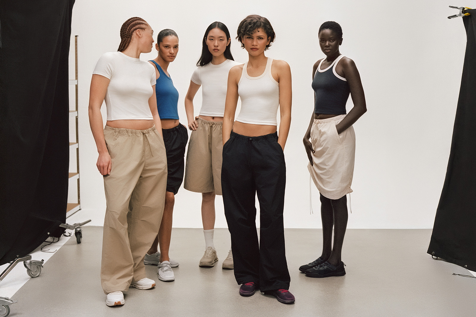 A still image from a fashion shoot for athletic brand On with actor Zendaya, who features wearing a white vest and black trousers, 2nd from the right with four other female models