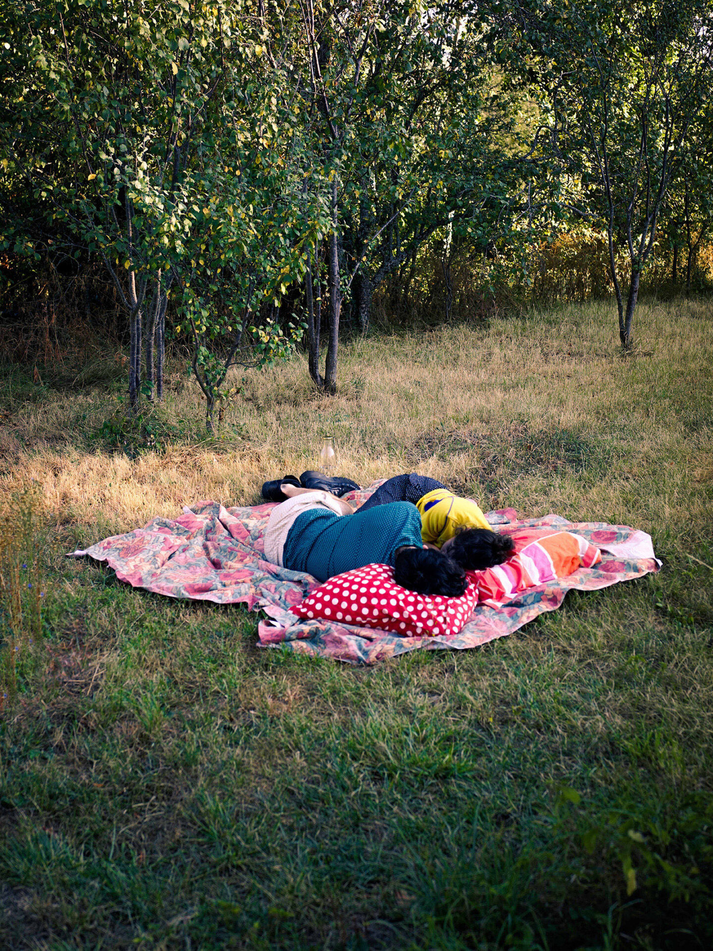 A photograph by Mayssa Jaoubat of an intimate moment between two people, who are lying facing each other, their heads on pillows, on a blanket lain over grass