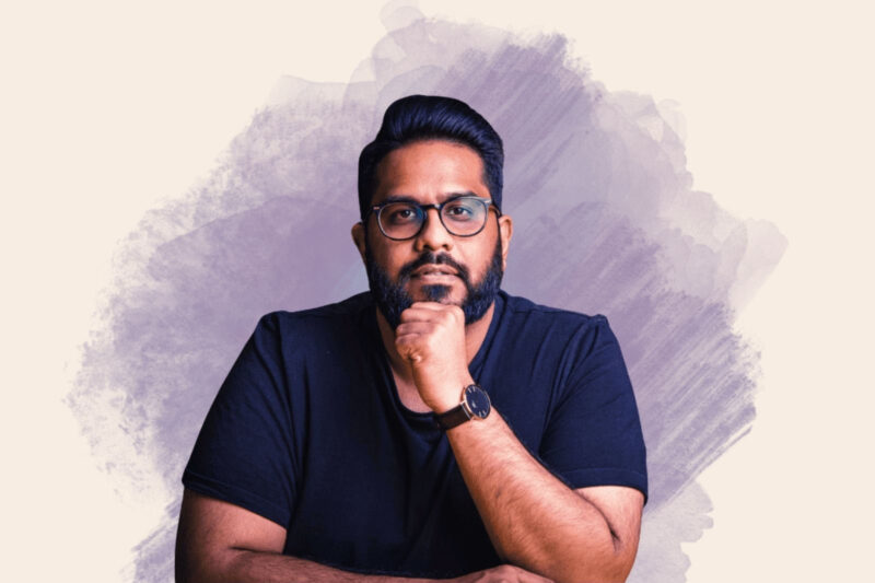 A composite image consisting of a portrait photo of Eshaan Akbar, wearing a dark T-shirt and with his chin resting on his left hand, overlaid on a neutral artwork background