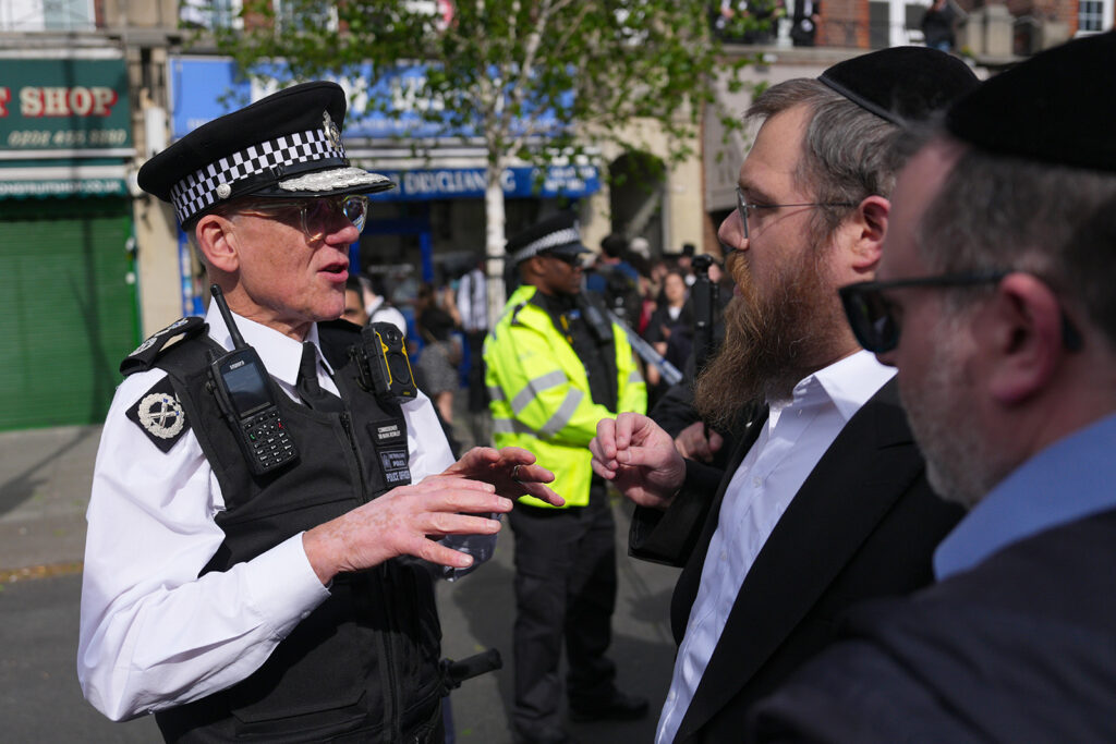 A man in police uniform addresses men in traditional Jewish dress