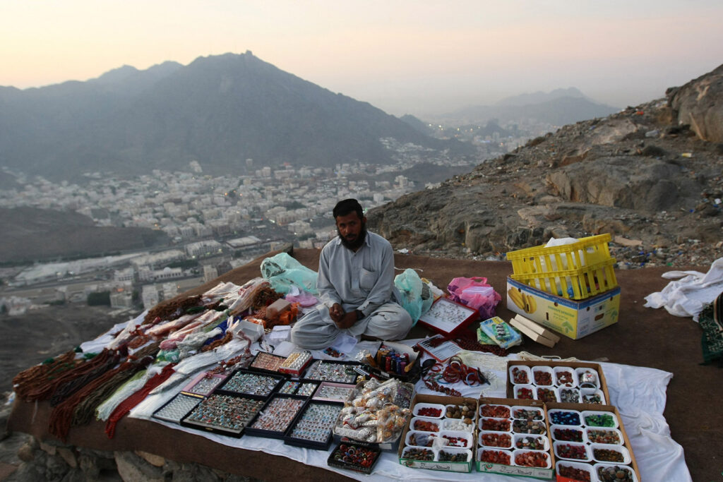 An early morning photograph of a man selling gifts for Muslim pilgrims on their way up Jabal al-Nour, with his wares laid out on a blanket on a rocky ledge on the mountainside