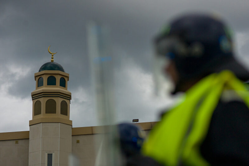 A photograph showing a police officer wearing a helmet and holding a riot shield, standing in front of a Sunderland mosque in August 2024, when Islamophobic riots targeted Muslim institutions across the UK