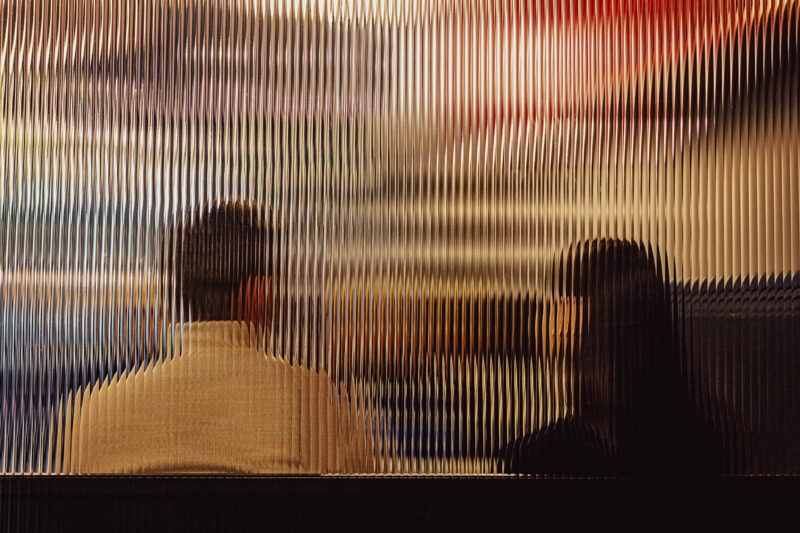 A stock image of a man and woman sitting beside each other, seen through a textured glass window