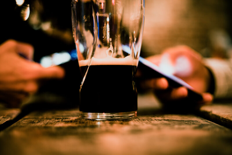 A close-up stock image of a half empty pint glass of beer on a bar