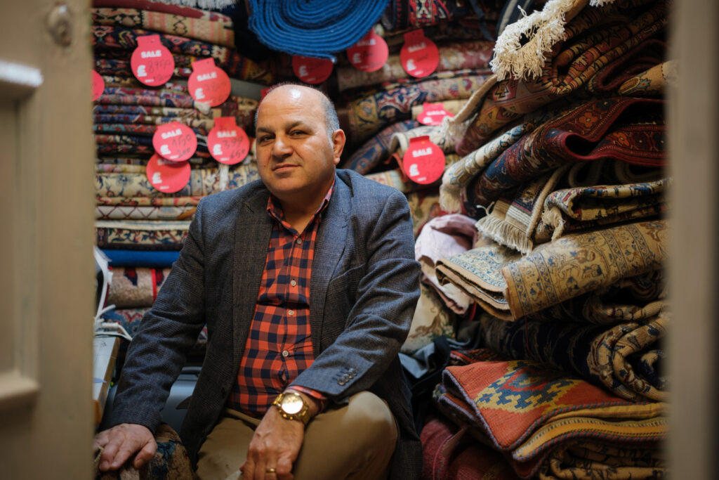 A photograph of Mostafa Lotfi in his cramped Queensway Market unit, which is piled high with the carpets he repairs and sells. He will be forced to relocate as a result of the closure of the market