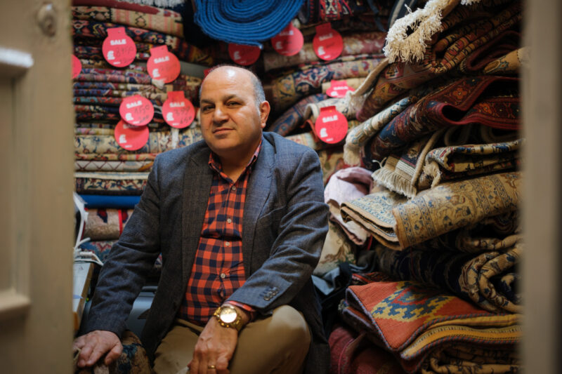 A photograph of Mostafa Lotfi in his cramped Queensway Market unit, which is piled high with the carpets he repairs and sells. He will be forced to relocate as a result of the closure of the market
