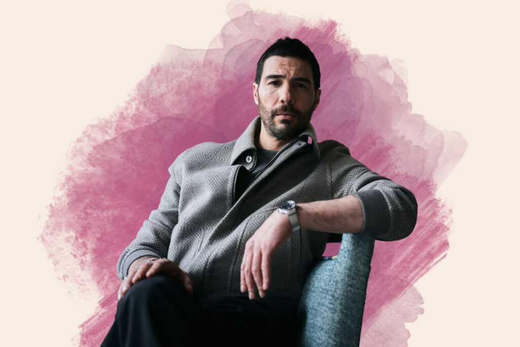 A composite image of French-Algerian actor Tahar Rahim, with a portrait photograph of him seated cross-legged, wearing a grey jacket, superimposed on a white and red background