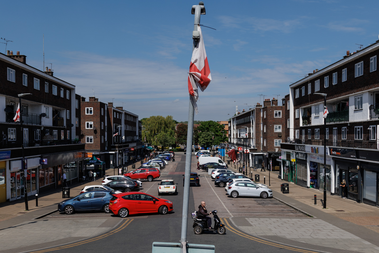 A faded St George flag hangs from a lamp post at the end of a street of shops in the Harold Hill area of Romford