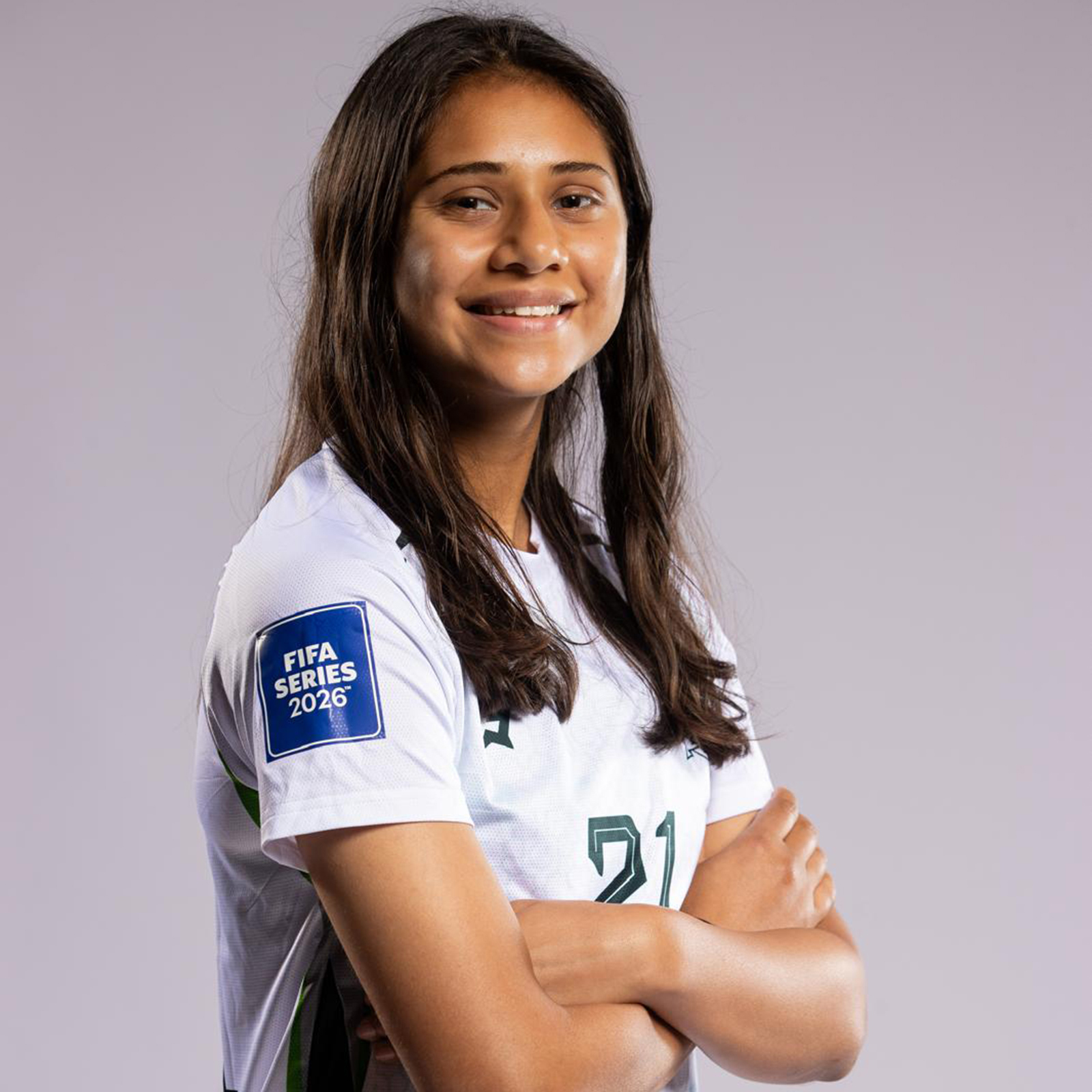 Zahmena Malik, her arms folded and her hair down, smiling, in a white shirt that reads FIFA SERIES 2026 with the number 21 on her front.