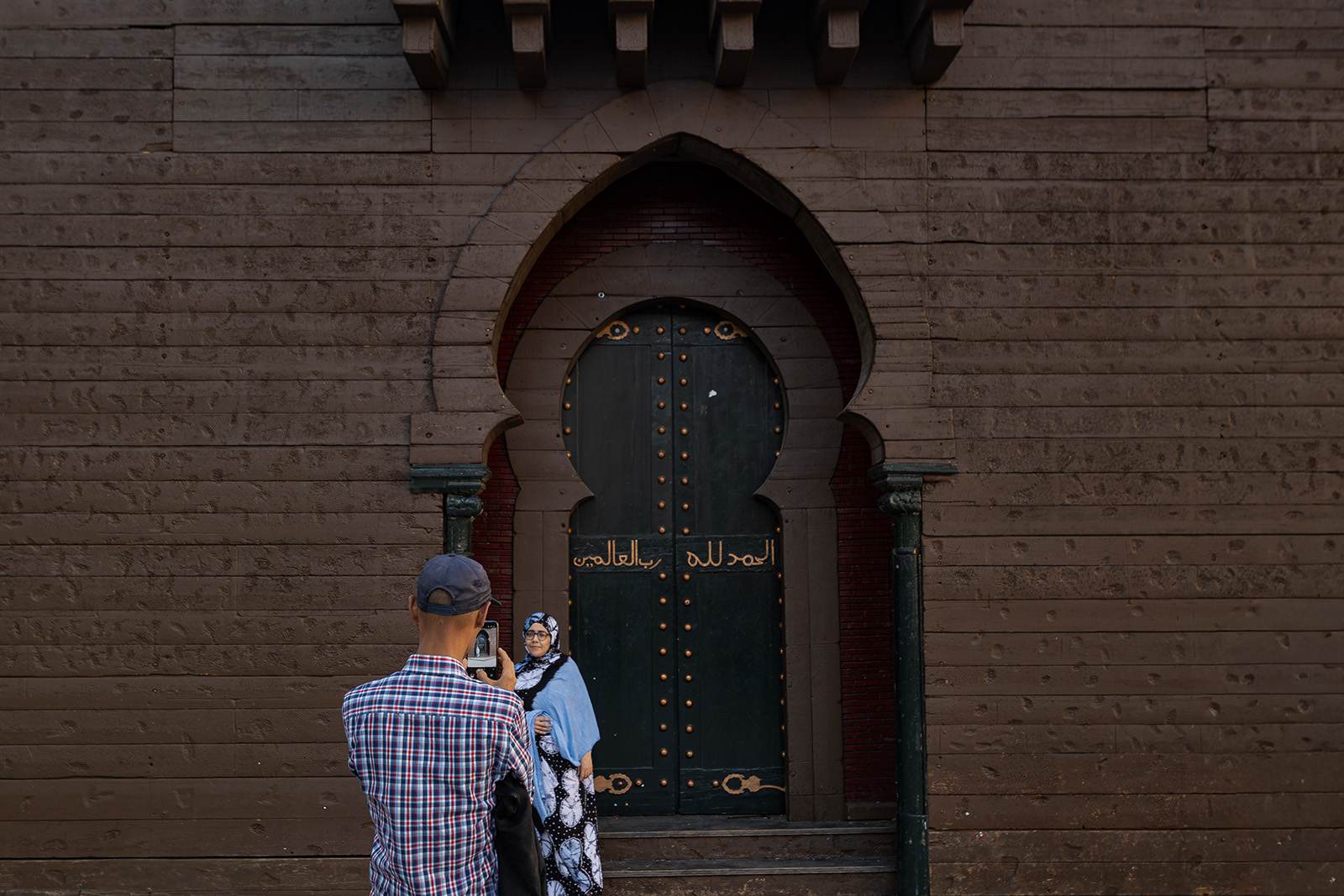 A woman poses for a photograph at the gates of the festival castle. The inscription, written in Arabic, reads: “Praise be to God, Lord of the Worlds.”