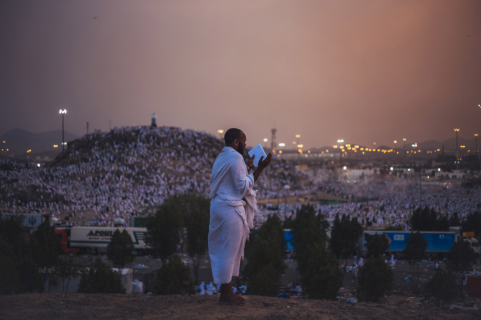 A pilgrim stands overlooking Mount Arafat at dusk during Hajj.