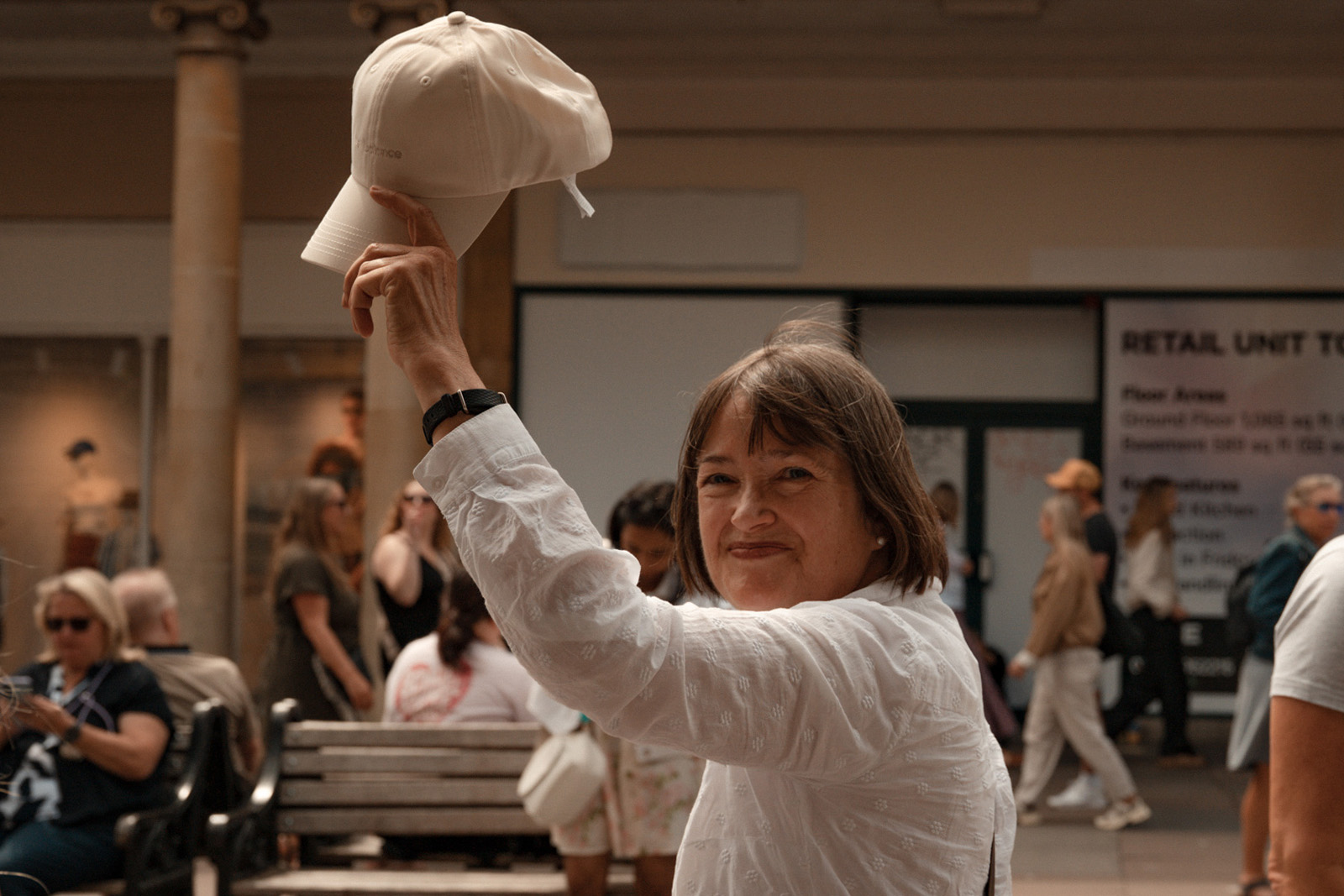 A photograph of a smiling Louise Rickitt, tour guide for the walk exploring Bath's history of welcoming refugees, looking directly at the camera and raising her cap in the air