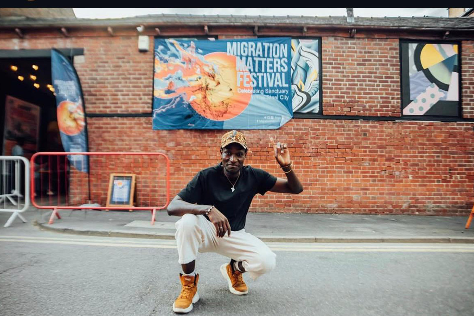 John Rwothomack, who is taking charge of his first Migration Matters Festival as director, kneeling in front of a banner ad promoting the festival