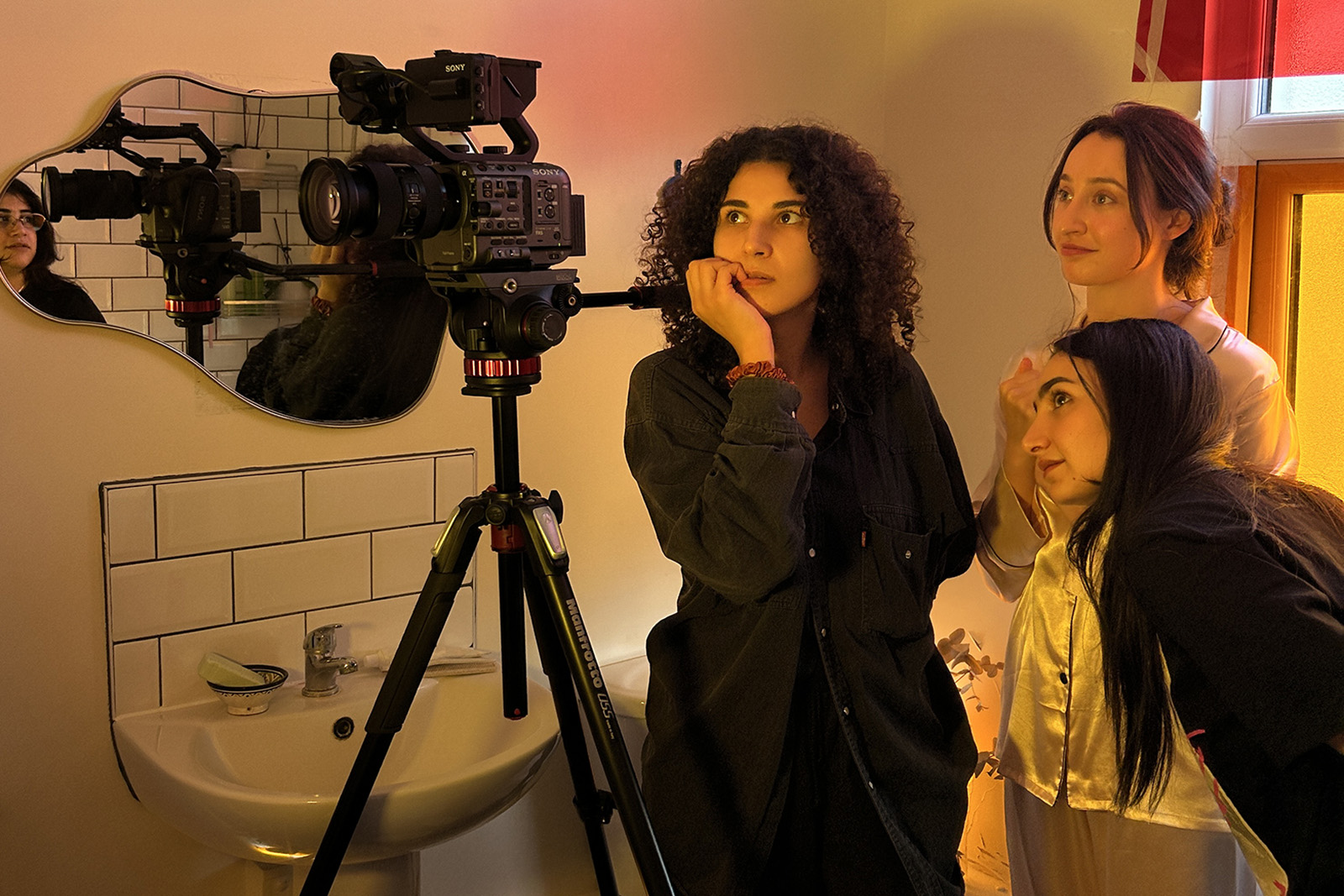 A photograph of Safia Lamrani (2nd from right) with two other women in a bathroom, with a camera on tripod to their right, on the set of the horror short she wrote and acted in, Late Tuesday Morning