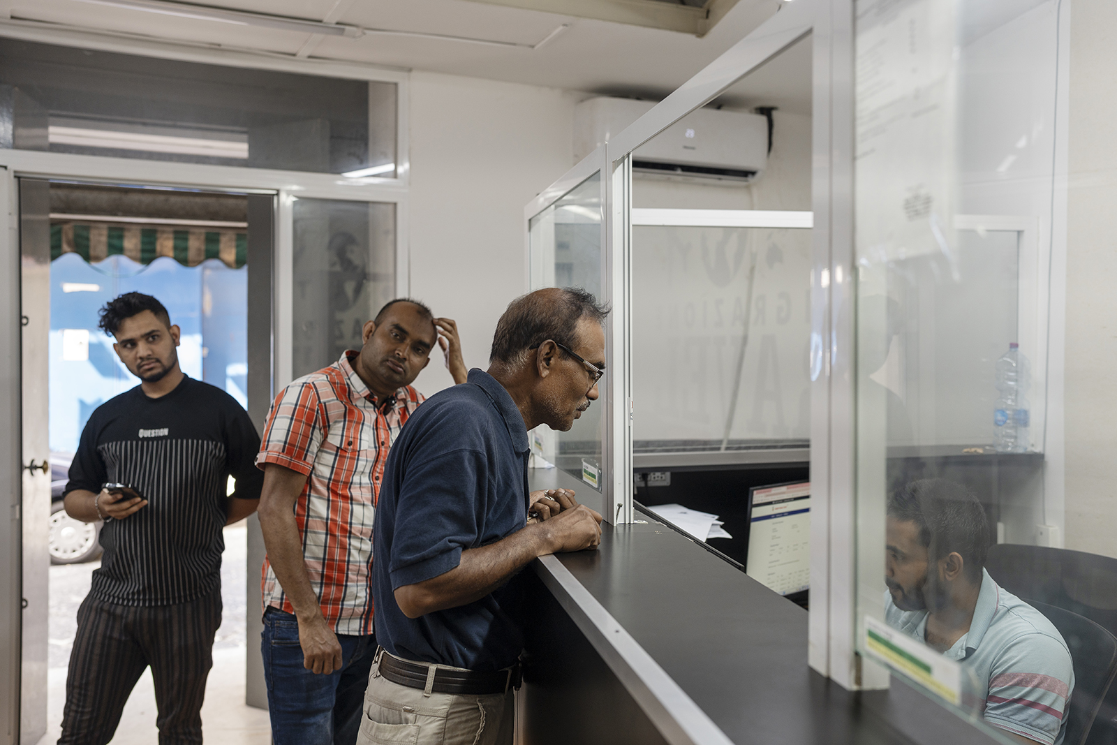 A photograph of Gias Uddin at a counter in the Bangladeshi consulate in Naples, asking an official about his Italian residence permit