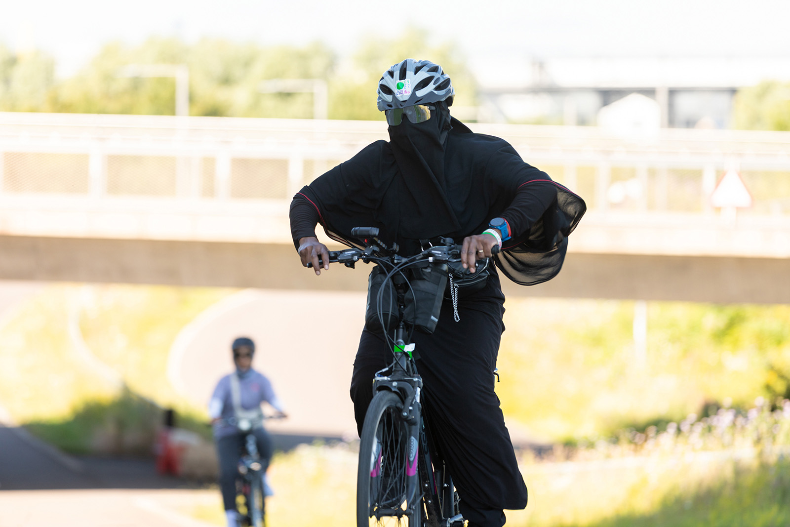 A photograph of a woman cycling with her whole body covered, including a face veil