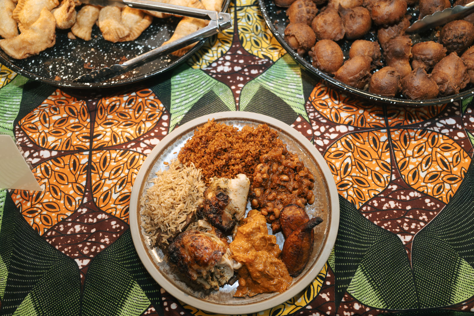 A photograph of plates of food from the buffet at Little Baobab's monthly teranga night, including (clockwise from top left) fish fataya pastries, beignets dougup and grilled chicken