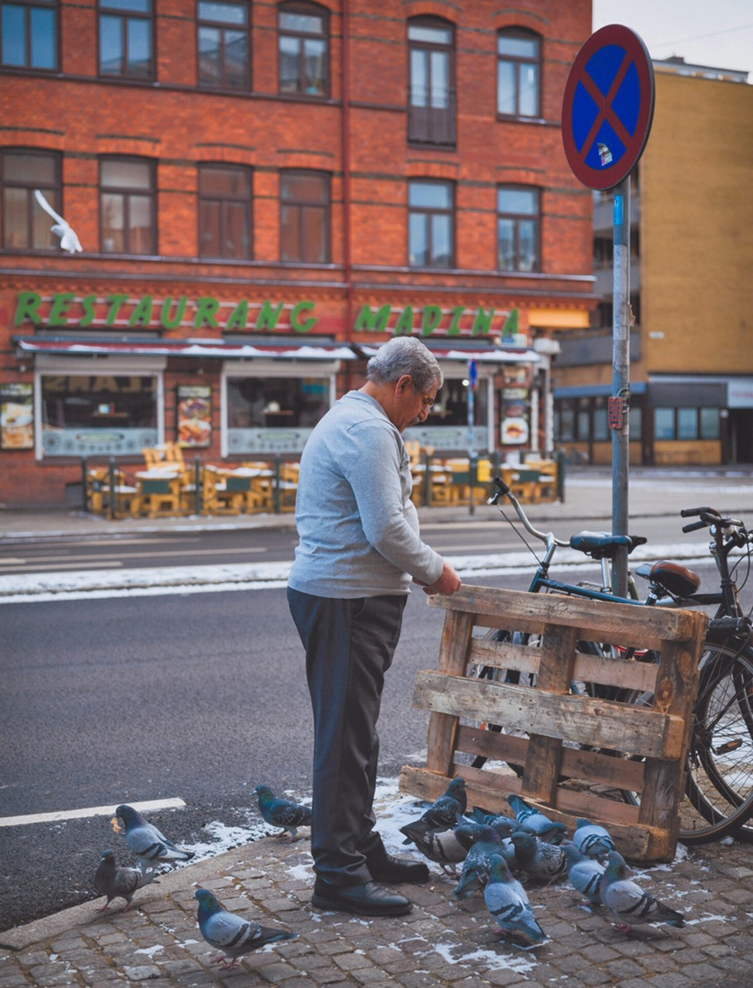 Photographer Ikram Abdulkadir's image of a man feeding pigeons, across the street from an eatery with prominent green Restaurang Madina signage