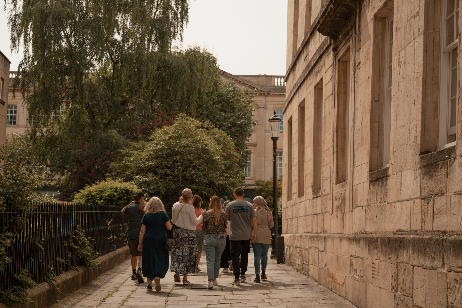 A photograph of the Bath refugee history tour group making its way around the city, walking away from the camera down a wide paved walkway with a Georgian building to the right and iron railings to the left