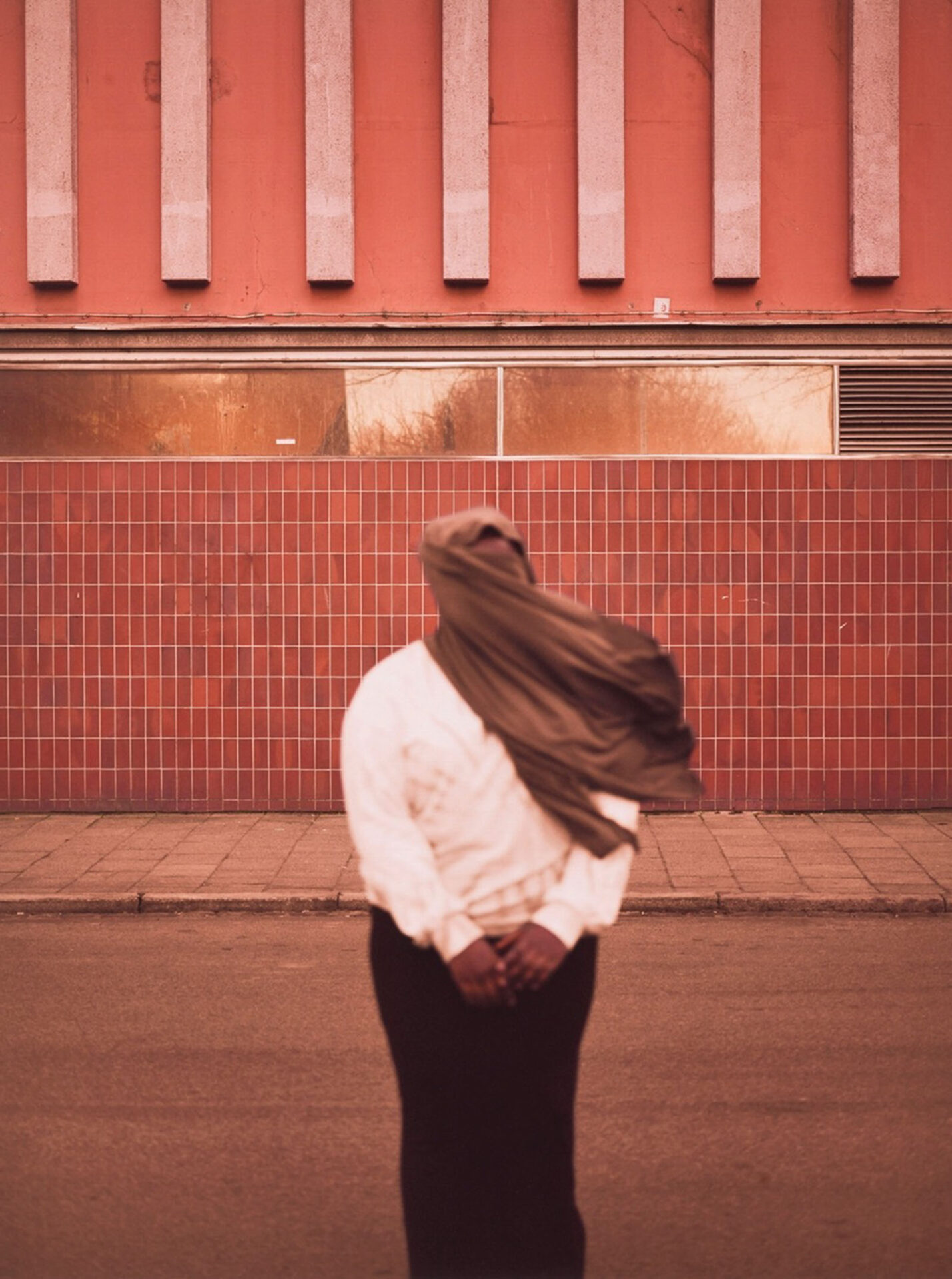 Photographer Ikram Abdulkadir's image of a woman standing in front of a red building, with her headscarf blowing in the wind and obscuring her face
