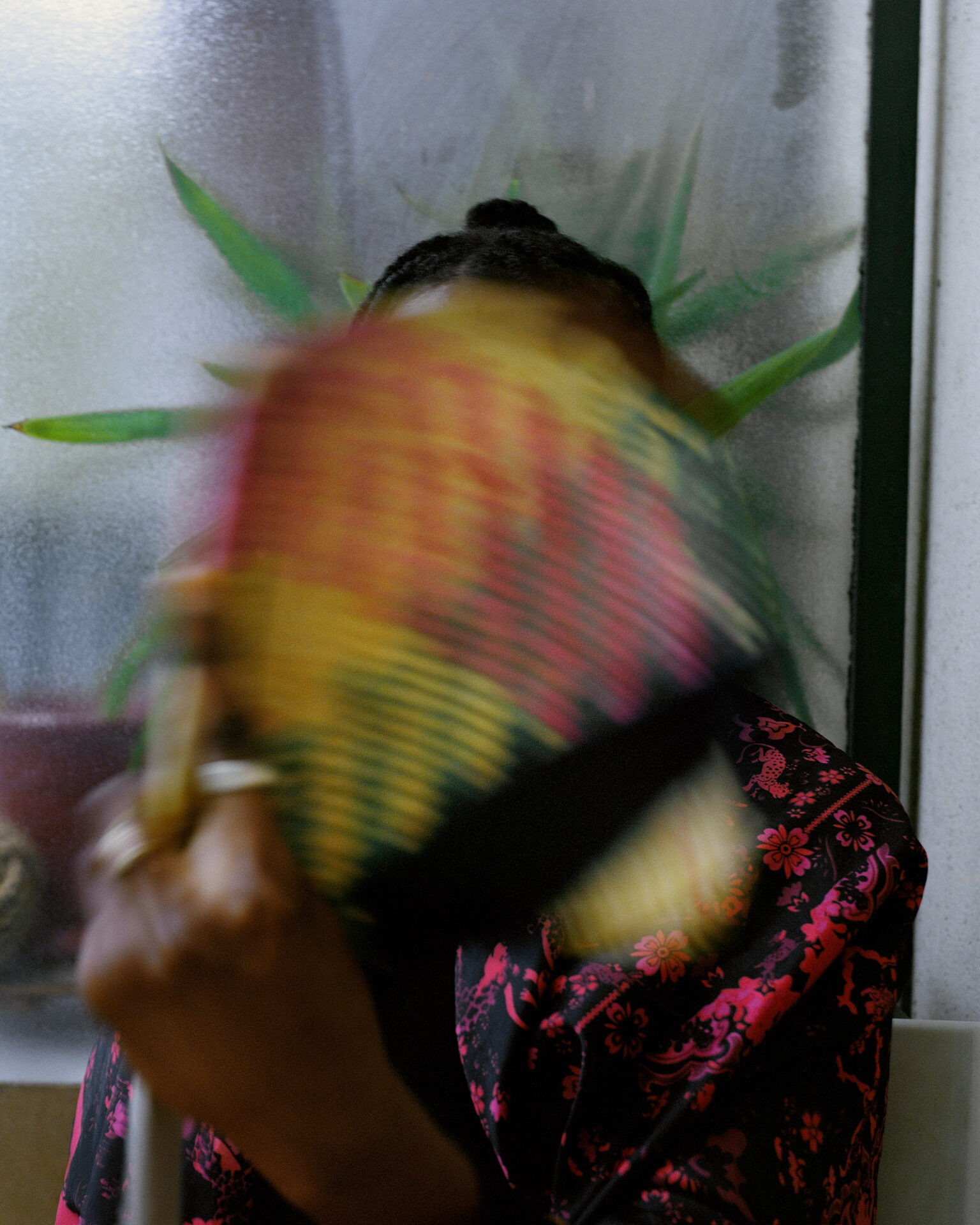 A portrait photograph, titled Awa, of someone apparently fanning themselves, with the blurred movement of the fan held in the person's left hand obscuring their face. From Camille Farrah Lenain’s monograph Made Of Smokeless Fire