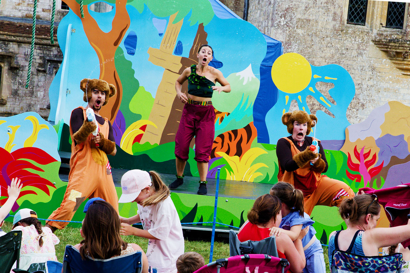 A performance of The Jungle Book by Immersion Theatre in the grounds of Athelhampton House, Dorset, June 2026, with two cast members in animal costumes swirting the audience with water pistols