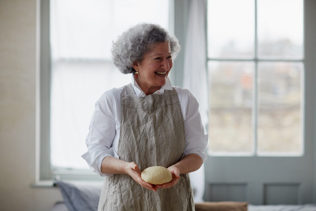 A photograph of Anissa Helou, smiling and wearing an apron while holding a ball of dough