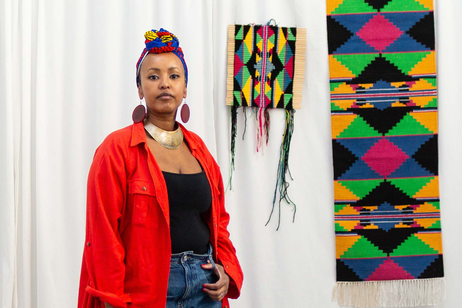 A portrait photograph of multidisciplinary British-Somali artist Fozia Ismail with some of her textile-based work