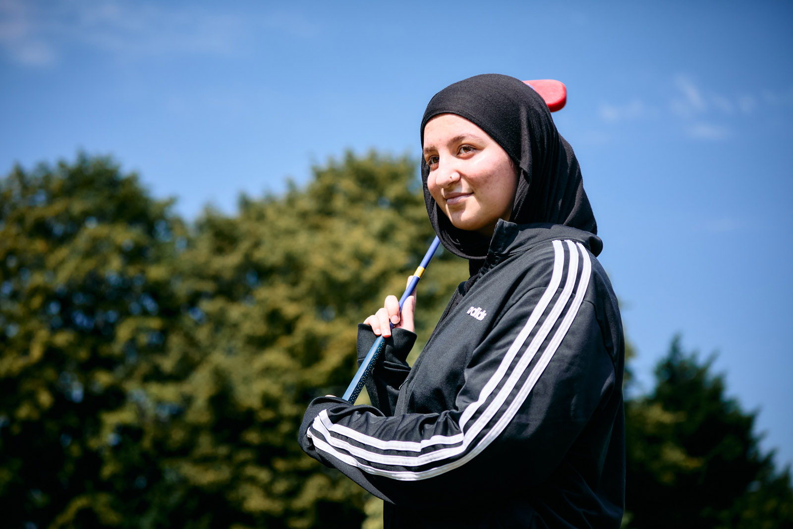 A stock photograph of a girl wearing a hijab and an Adidas tracksuit top holding a golf club