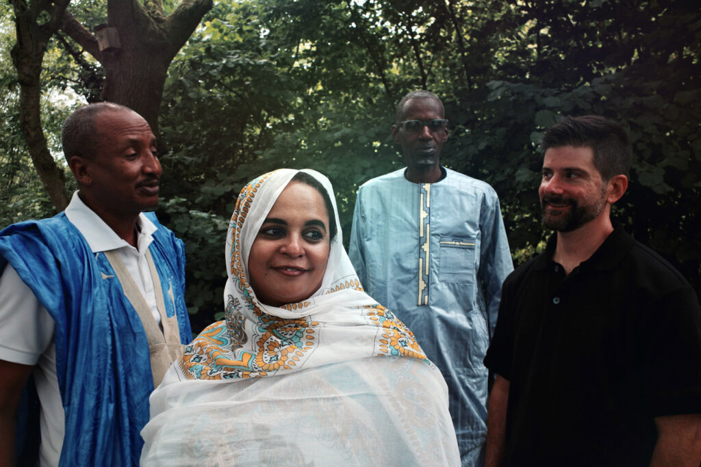 A publicity photo of Noura Mint Seymali with her band, husband and guitarist Jeich Ould Chighaly (left), bassist Ousemane Tour and drummer/producer Matthew Tinari (right)