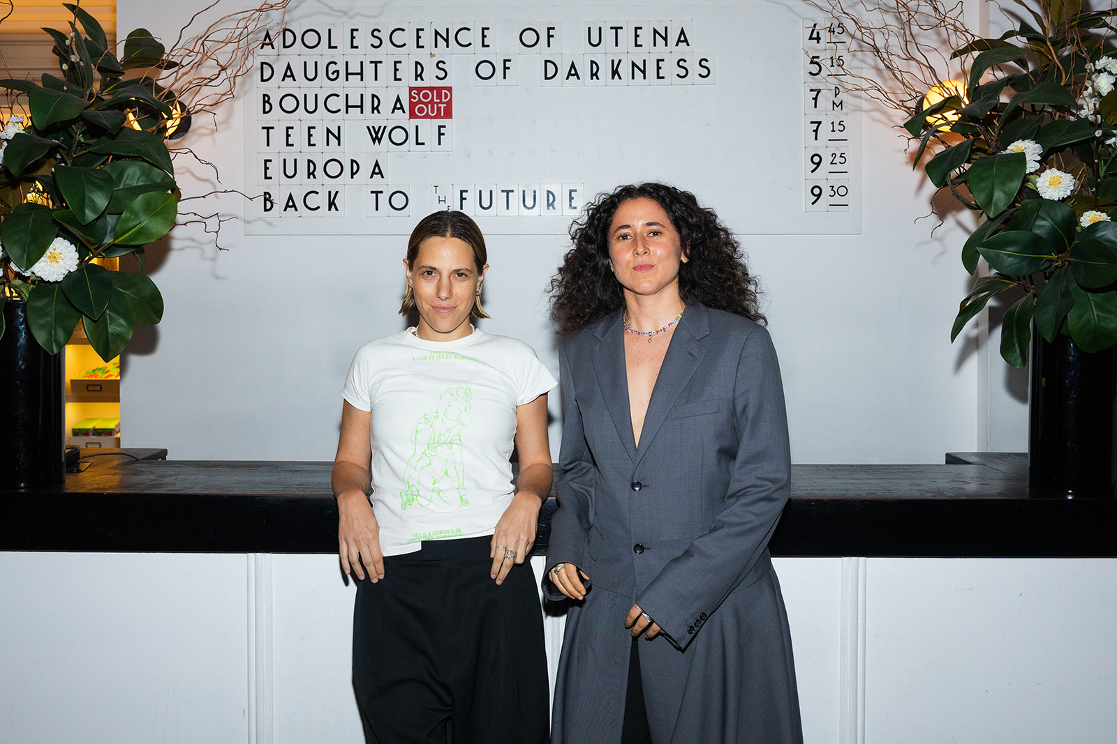 A photograph of Orian Barki (left) and Meriam Bennani, taken in a cinema foyer, with their film Bouchra shown as 'sold out' on the list of screening times on the wall behind them