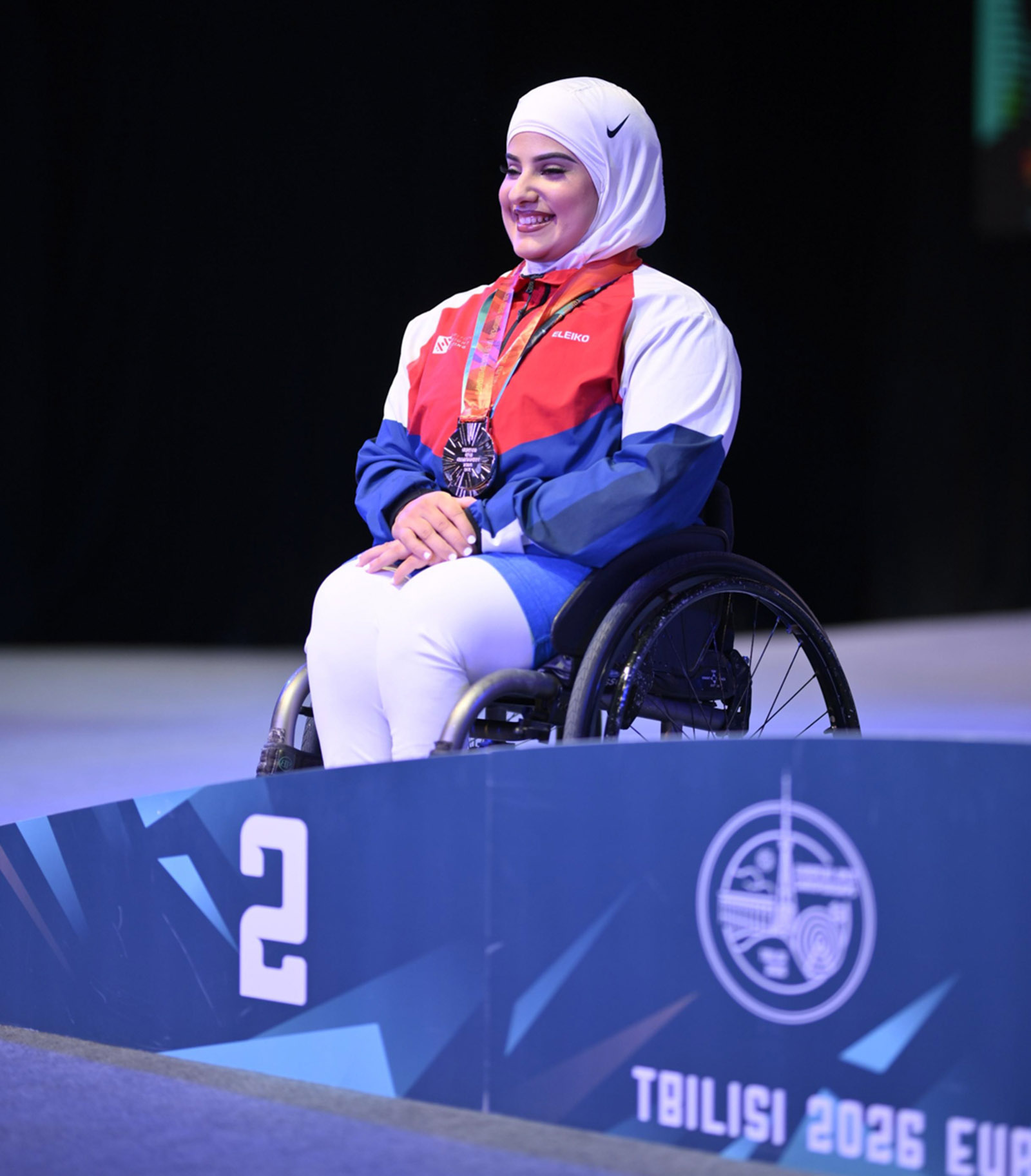 A photograph of Doaa Shayea smiling and wearing the silver medal she won in the women's 67kg category para powerlifting silver medal at the European Championships in Georgia, March 2026