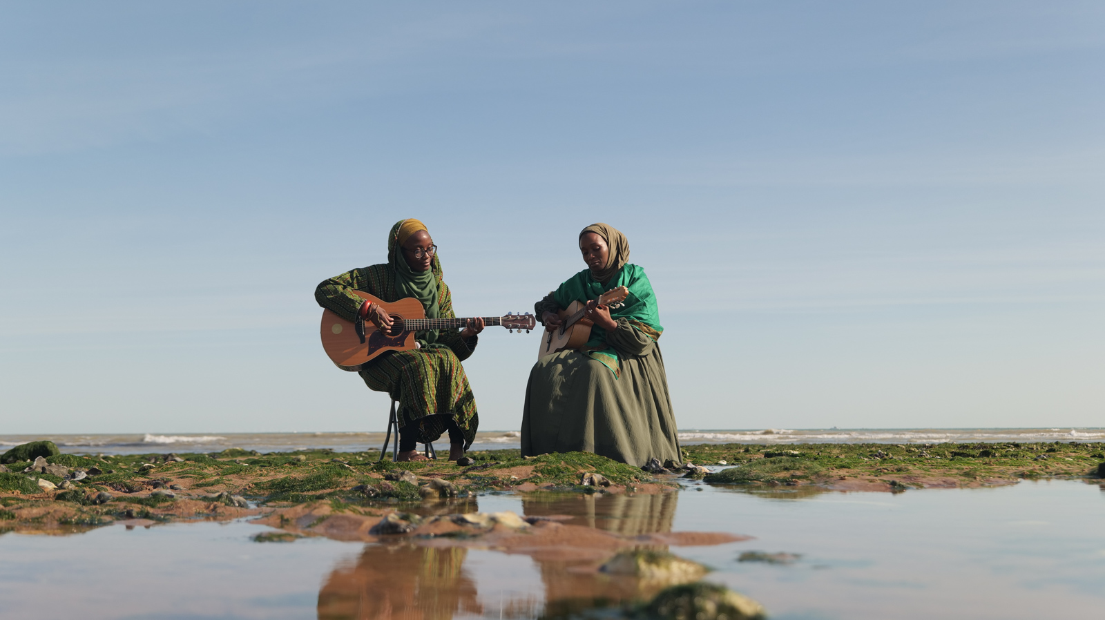 A photograph of Pearls of Islam playing guitars while sitting on a beach