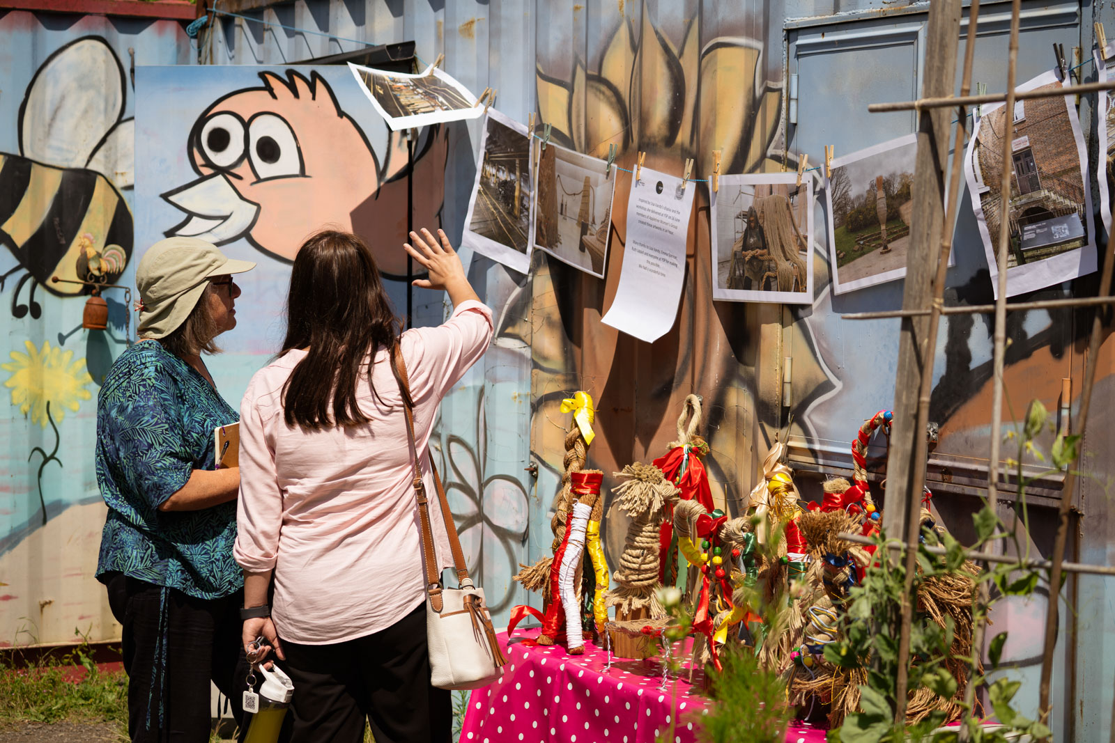 A photograph of two women in Appletree Community Garden looking at decorative items made from rope and pictures of the work of artists Lisa Vandy, which provided the inspiration
