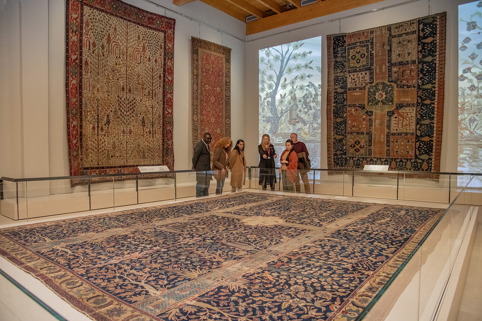 A photograph of visitors viewing the Wagner Carpet display, which fills most of the room and is protected by a glass partition, at The Burrell Collection, Glasgow