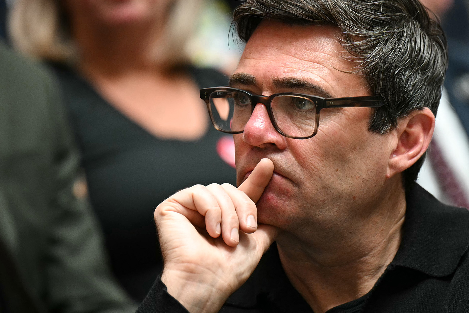 A close-up photograph of Andy Burnham, one finger of his right hand resting on his mouth as he listens at the Labour 2024 general election manifesto launch in Manchester