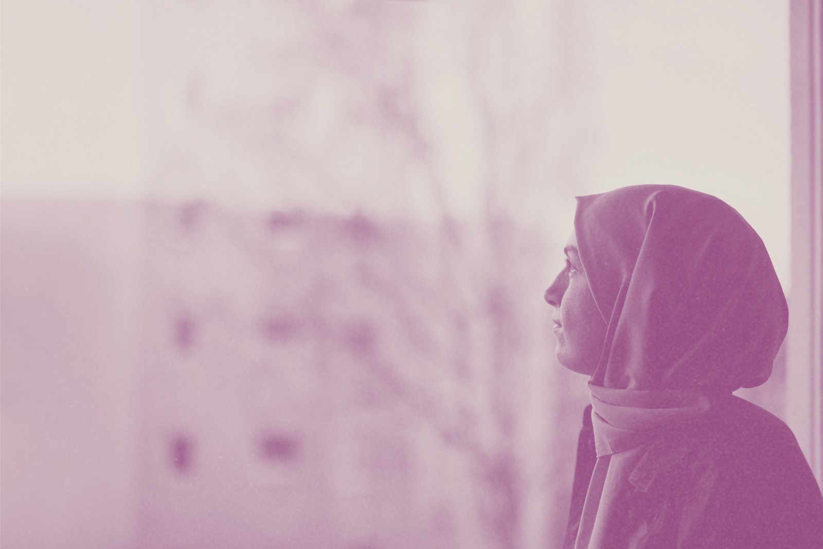 A stock image of a thoughtful women wearing a headscarf looking out of a window