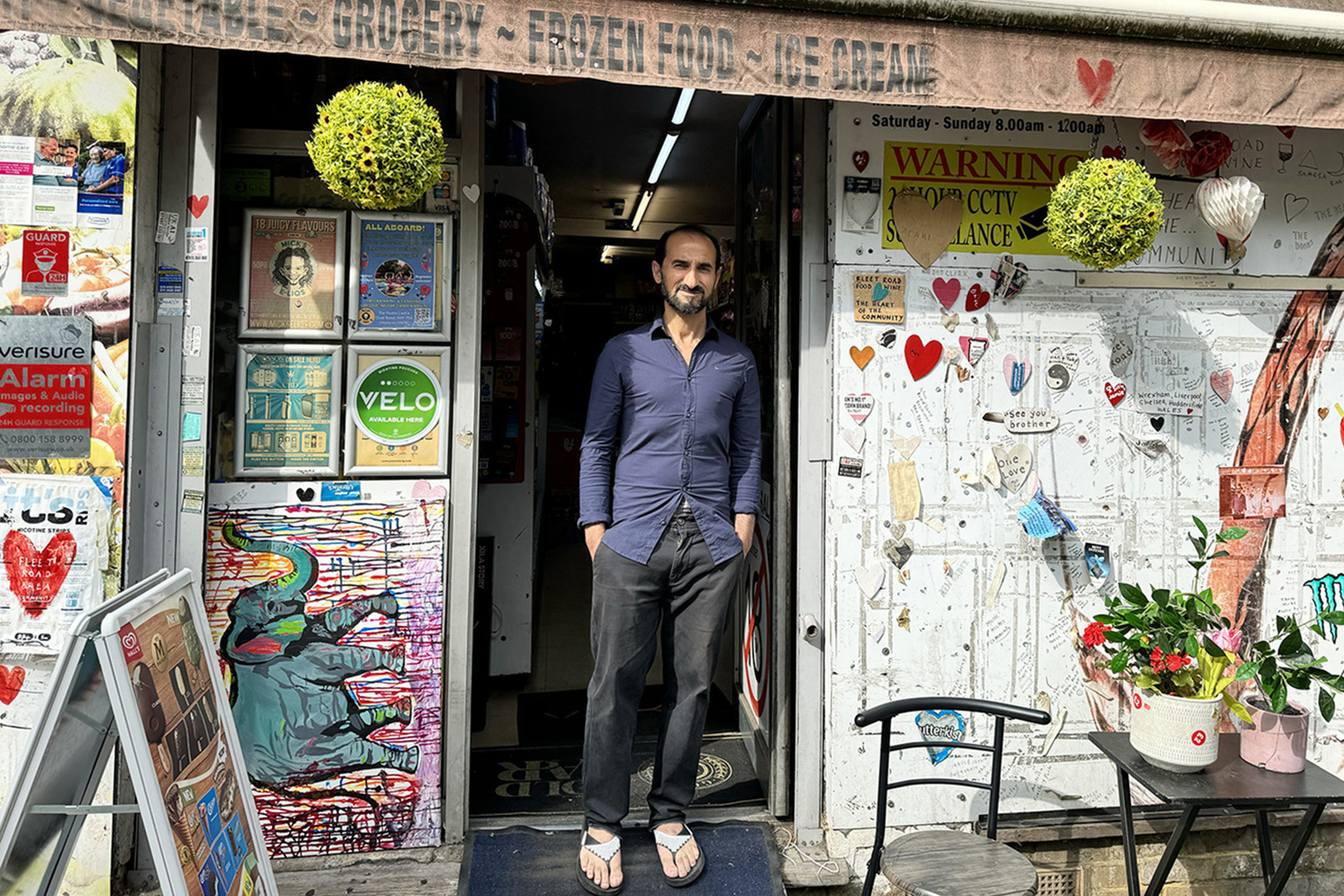 A photograph of Abdul Safy, smiling and wearing flip-flops, at the door of Fleet Food and Wine, Belsize Park, north London, on a sunny day