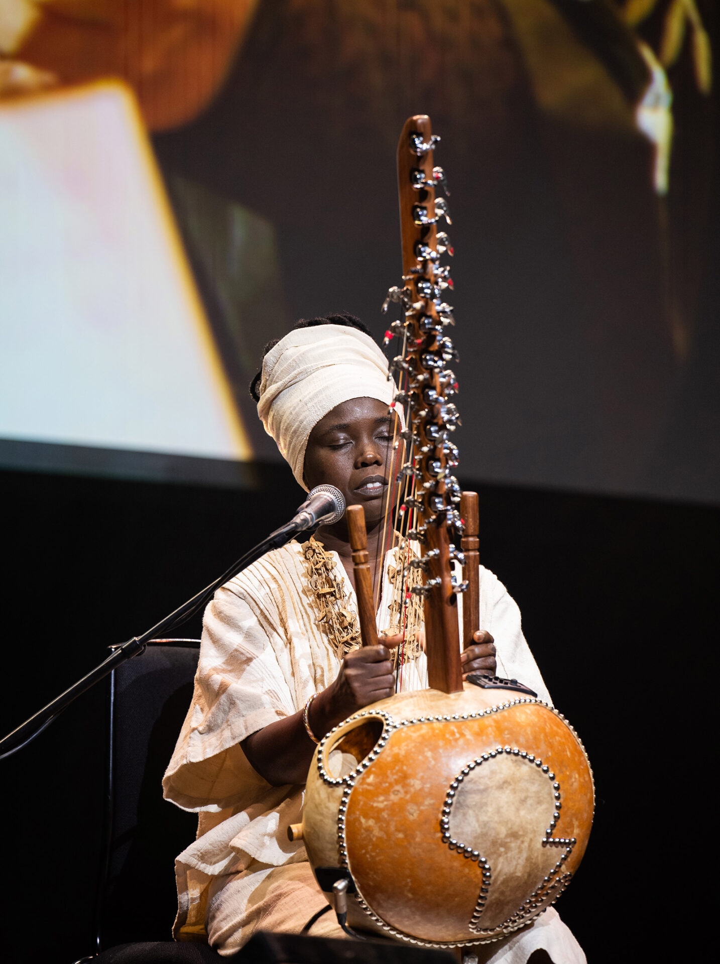 A photograph of Senegalese musician Senny Camara on stage playing a kora