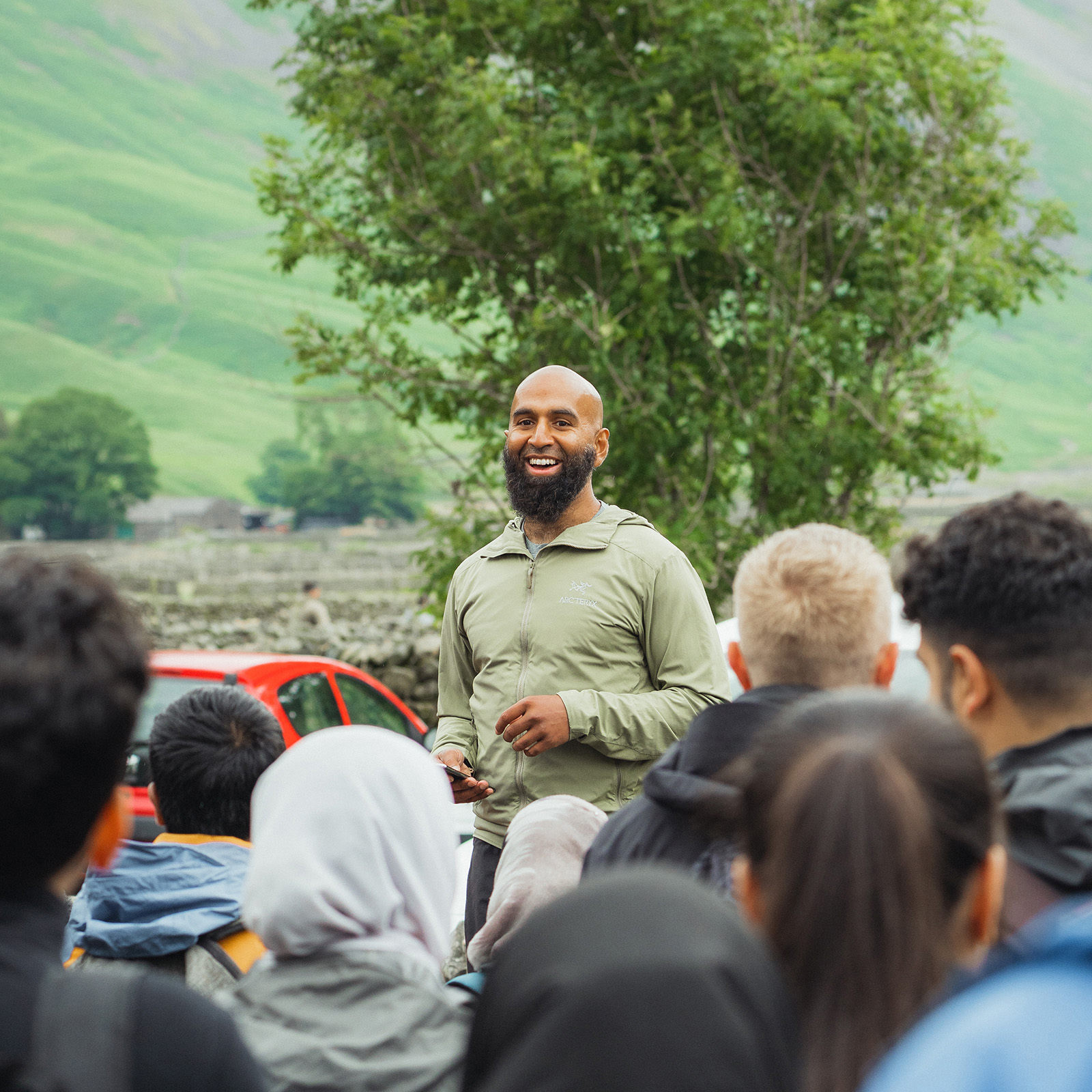 A photograph of a smiling Haroon Mota talking to a Muslim Hikers group in the Lake District before they tackle Scafell Pike, the highest peak in England, July 2023