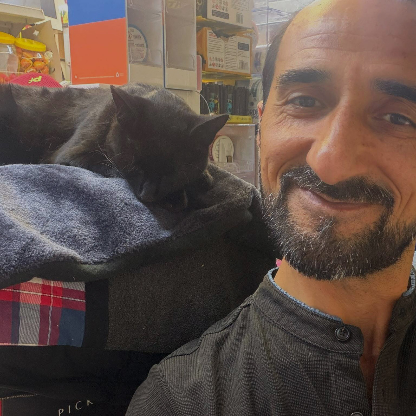 What appears to be a selfie taken by Abdul Safy inside his shop, with his cat Mimi resting on a blanket over his right shoulder