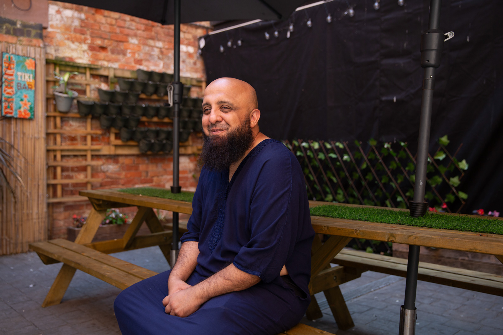 A man with a beard smiles, sitting on a picnic bench