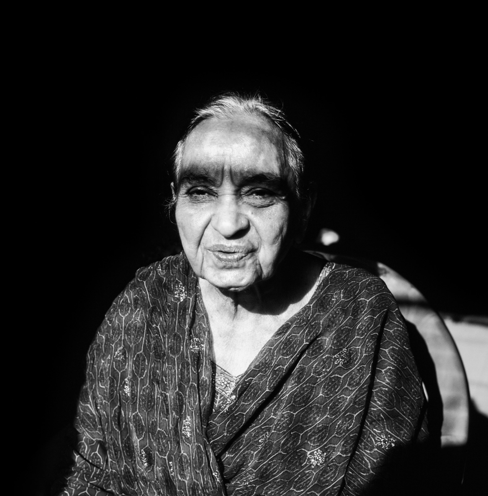 A black and white photograph from Aman Alam's series Ozymandias, documenting his grandmother's life with Alzheimer's, titled Naseem in the Sun. Sunbathing in the winter sun during the second Covid lockdown. Sunlight on her body always cheers her up.